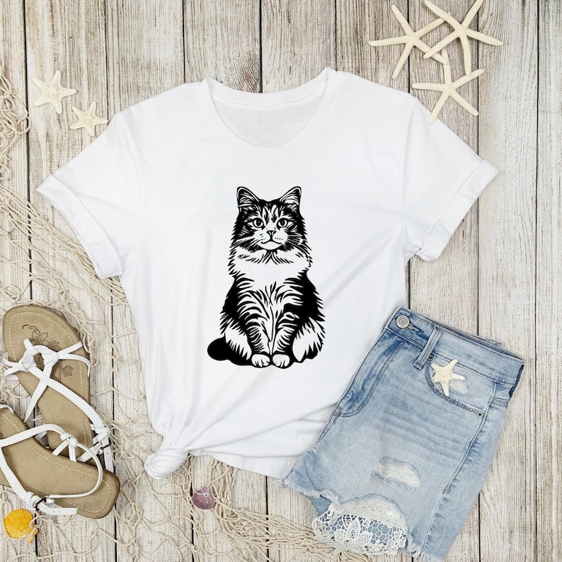 May include: White t-shirt featuring a black and white illustration of a cat sitting on a white background.