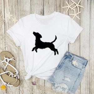 May include: White t-shirt with a black silhouette of a dog jumping in the air.