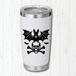 K&ouml;nnte beinhalten: Wei&szlig;er Reisebecher mit einem schwarzen Fledermaus-, Totenkopf- und gekreuzten Knochen-Design. Der Edelstahlbecher hat einen silbernen Deckel und Boden. Das gruselige Design ist perfekt f&uuml;r Halloween oder Gothic-Themen.