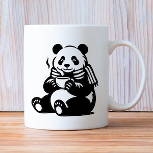 May include: White ceramic mug featuring a black and white illustration of a panda bear. The panda is wearing a scarf and holding a cup, with steam rising from it. The mug has a curved handle and is set against a wooden background.