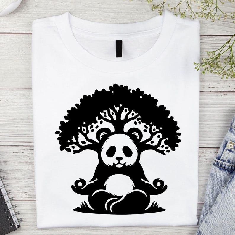 May include: White t-shirt featuring a black graphic of a panda meditating under a tree. The panda is in a lotus position, with the tree's branches forming a canopy above its head. The design is centered on the shirt.