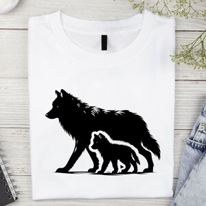 May include: Black silhouette of a wolf and a wolf pup walking side by side on a white t-shirt.