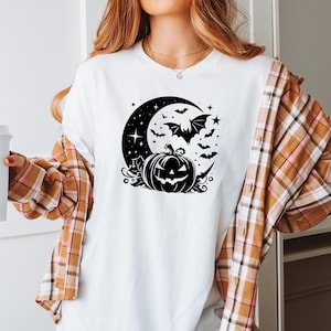 K&ouml;nnte beinhalten: Wei&szlig;es T-Shirt mit einem schwarzen Halloween-Design. Die Grafik zeigt einen Halbmond, Flederm&auml;use, Sterne und einen geschnitzten K&uuml;rbis. Teil einer Halloween-Kollektion.