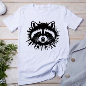 May include: White t-shirt with a black and white graphic of a raccoon's face.