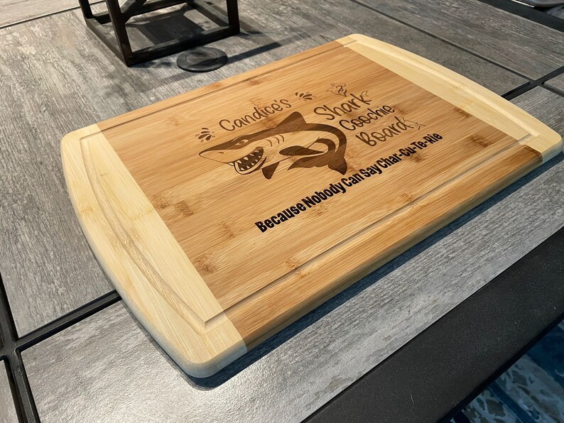 Puede incluir: Una tabla de cortar de bamb&uacute; personalizada con un gr&aacute;fico de tibur&oacute;n y el texto "Candice's Shark Coochie Board Because Nobody Can Say Char-Cu-Te-Rie".