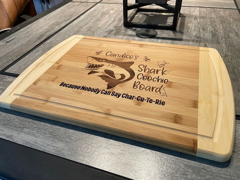 Puede incluir: Una tabla de cortar de bamb&uacute; personalizada con un gr&aacute;fico de tibur&oacute;n y el texto "Candice's Shark Coochie Board Because Nobody Can Say Char-Cu-Te-Rie".