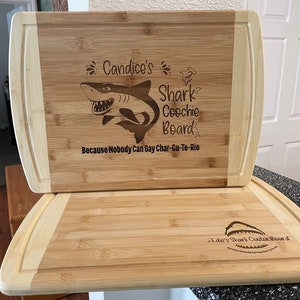 Puede incluir: Dos tablas de cortar de bamb&uacute; personalizadas con un dise&ntilde;o de tibur&oacute;n. La tabla superior dice "Candice's Shark Coochie Board Because Nobody Can Say Char-Cu-Te-Rie". La tabla inferior dice "Edie's Shark Coochie Board".