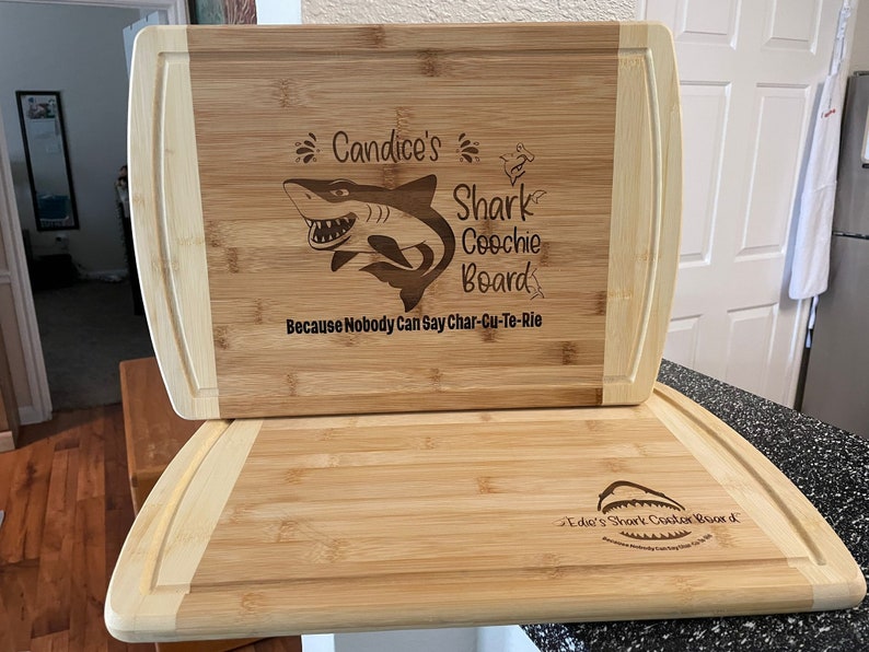 Puede incluir: Dos tablas de cortar de bamb&uacute; personalizadas con un dise&ntilde;o de tibur&oacute;n. La tabla superior dice "Candice's Shark Coochie Board Because Nobody Can Say Char-Cu-Te-Rie". La tabla inferior dice "Edie's Shark Coochie Board".