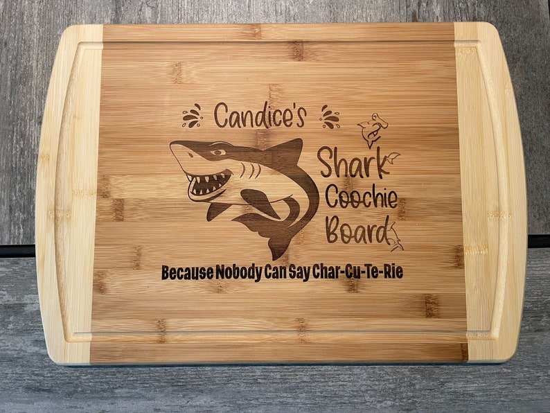 Puede incluir: Una tabla de cortar de bamb&uacute; personalizada con un gr&aacute;fico de tibur&oacute;n y el texto "Candice's Shark Coochie Board Because Nobody Can Say Char-Cu-Te-Rie".