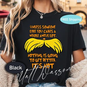 Könnte beinhalten: Schwarzes T-Shirt mit dem Zitat "Unless someone like you cares a whole awful lot, nothing is going to get better. It's not." Das Shirt zeigt eine gelbe Schnurrbart-Grafik und den Namen "Matt Wasson".
