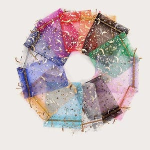 Peut inclure: Un ensemble de 12 petits sacs en organza transparent avec des paillettes dor&eacute;es et un motif de croissant de lune et d'&eacute;toiles. Les sacs sont de diff&eacute;rentes couleurs, notamment rose, bleu, violet et vert.