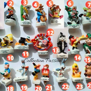 May include: A collection of twenty-five small Looney Tunes character figurines made of painted material, each mounted on a white base with printed text. The figures depict various animated characters in different poses, colors, and outfits.