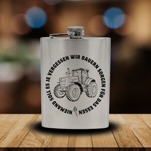 Op de afbeelding: Een zilveren roestvrijstalen drinkfles met een zwart-wit ontwerp van een tractor en de tekst "Niemand soll es je vergessen wir Bauern sorgen für das Essen".