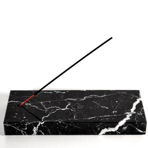 Könnte beinhalten: Schwarzer Marmor-Räucherstäbchenhalter mit einem schwarzen Räucherstäbchen darauf.