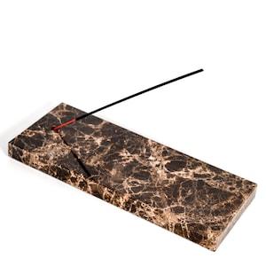 Könnte beinhalten: Ein brauner Marmor-Räucherstäbchenhalter mit einem schwarzen Räucherstäbchen darauf.