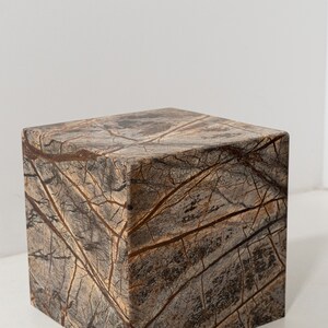 May include: A square, brown marble pedestal with a light brown and dark brown marbled pattern.