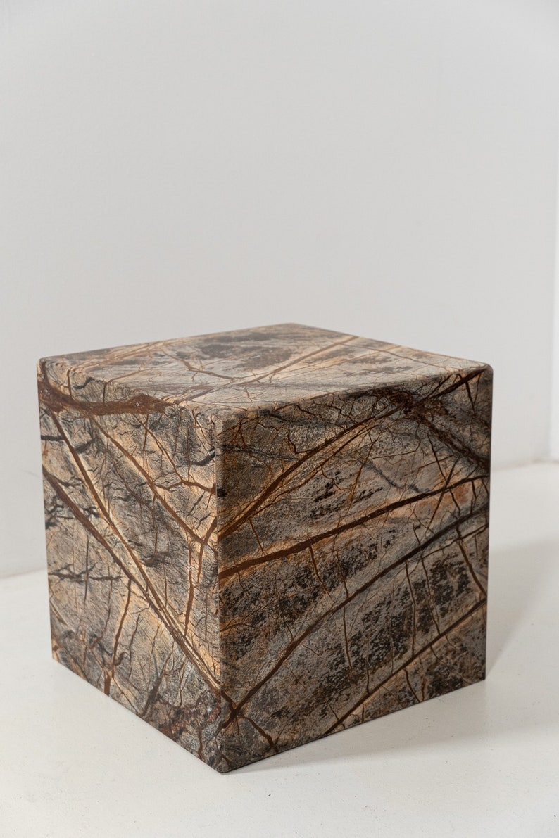 May include: A square, brown marble pedestal with a light brown and dark brown marbled pattern.