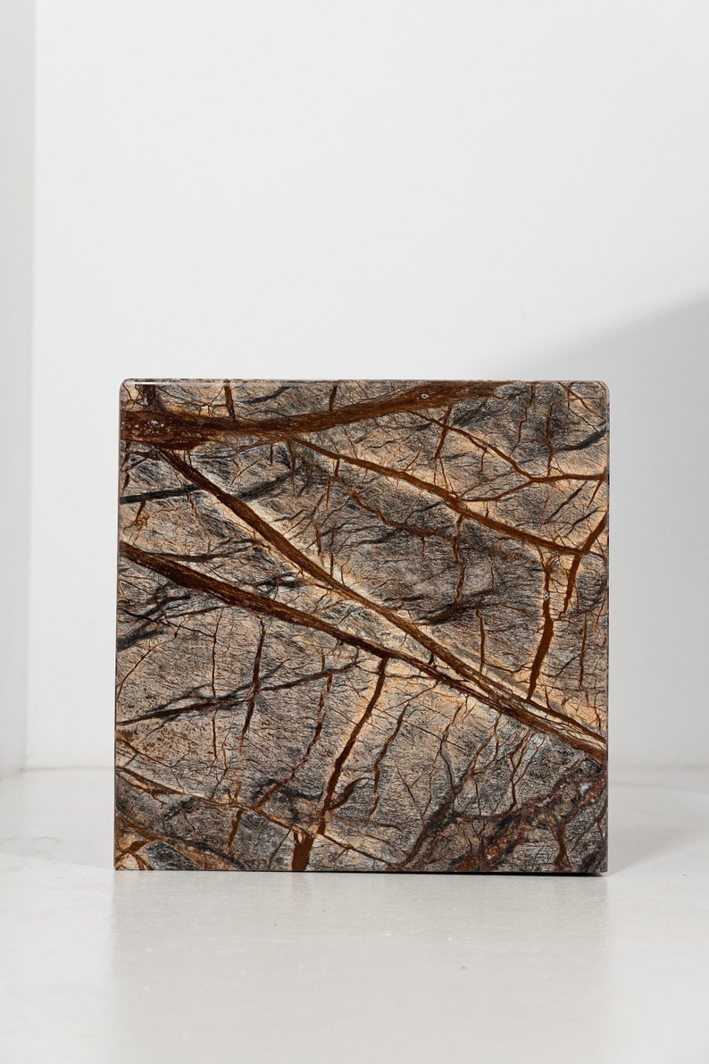 May include: A square, brown and gray marble tile with a natural veined pattern.
