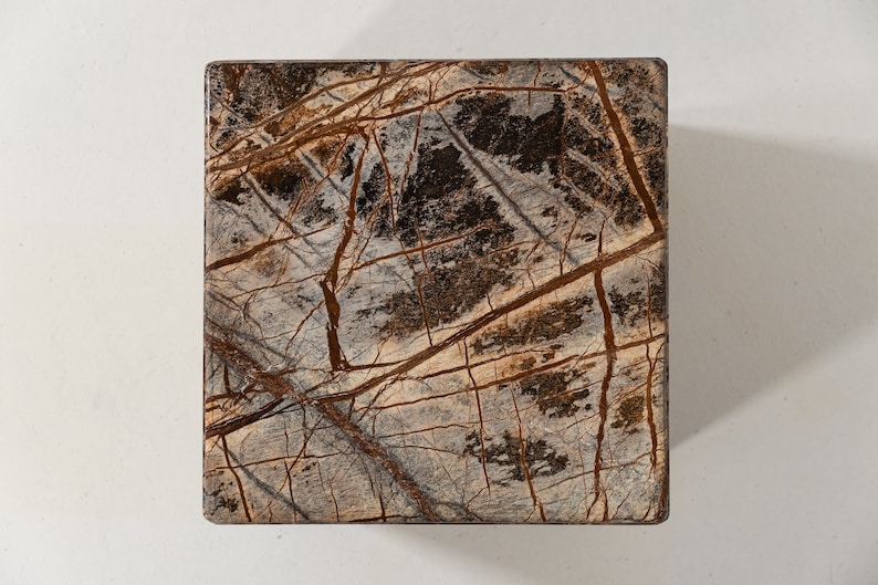 May include: A square, brown and gray marble tile with a natural veined pattern.