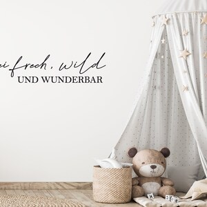 May include: A nursery scene featuring a light grey canopy bed with star decorations. A teddy bear sits beside a woven basket and a small rug. The wall displays the text "Sei frech, wild und wunderbar."