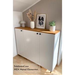 Beispiel für ein Projekt mit einer Massivholzdeckplatte nach Maß aus Eiche von Omformo. Hier als DIY Sideboard mit IKEA Metod Elementen, Möbelfüßen Upp in 10 cm Höhe und Möbelknöpfe Platta in Schwarz von Omformo. Dekoriert mit Pflanzen, einer weißen Vase mit Pampasgras und einer beigen Pilzlampe um ein Wohnbeispiel für einen modernes Sideboard darzustellen.