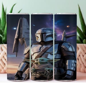 K&ouml;nnte beinhalten: Ein Edelstahlbecher mit einer detaillierten Illustration von The Mandalorian und Grogu, vor einer Weltraumszene mit einem Raumschiff. Das Design umfasst eine Figur mit Helm und einen kleinen gr&uuml;nen Au&szlig;erirdischen. Der Becher ist zylindrisch.
