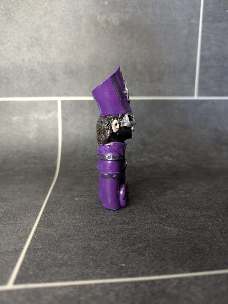 May include: Purple and black figurine of a character wearing a tall hat with a skull face mask.