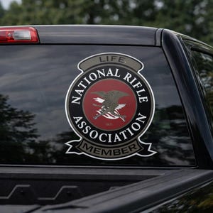 Puede incluir: Una taza de cerámica blanca con asa negra y el texto "But First, Coffee" en negrita negra. La taza se encuentra sobre un fondo borroso, sugiriendo un ambiente acogedor.