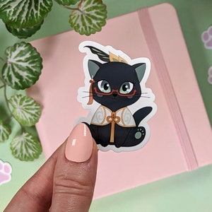 May include: A black cat wearing glasses and a gold and white patterned robe. The cat is wearing a red headband with a feather. The cat is sitting on a pink background.