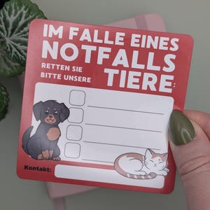 May include: A red and white pet emergency contact card with the text "IM FALLE EINES NOTFALLS RETTEN SIE BITTE UNSERE TIERE:" and illustrations of a dog and a cat. Includes space for contact information.
