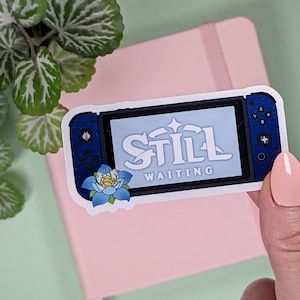 May include: A blue and white sticker of a Nintendo Switch console with the text "Still Waiting" on the screen. A blue flower is in the bottom left corner of the sticker.