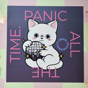 May include: A square print with a white cat holding a disco ball, with the text "Panic All The Time." The cat has a worried expression. The background is dark purple with pink text and yellow star accents.