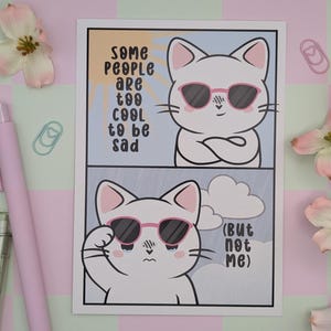 Op de afbeelding: Illustratie van een witte kat met een zonnebril, met de tekst "Some people are too cool to be sad" en "(But not me)". De kat wordt in twee panelen afgebeeld, één vrolijk en één verdrietig, tegen een blauw-gele achtergrond.