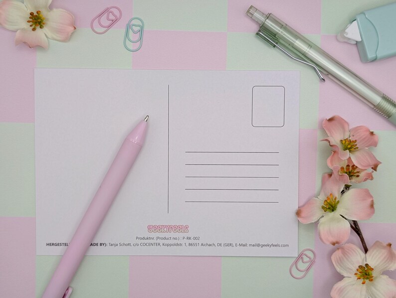 May include: A blank postcard with lines for addressing and a stamp box, alongside a pink pen, a green mechanical pencil, and a light blue eraser. The postcard is surrounded by pink and white flowers, and pink and green paperclips.