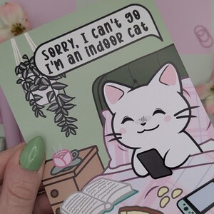 May include: A greeting card with a cartoon cat in bed holding a phone. The card has the text "Sorry, I can't go, I'm an indoor cat" in a speech bubble. The card is light green with a pink and white patterned background.