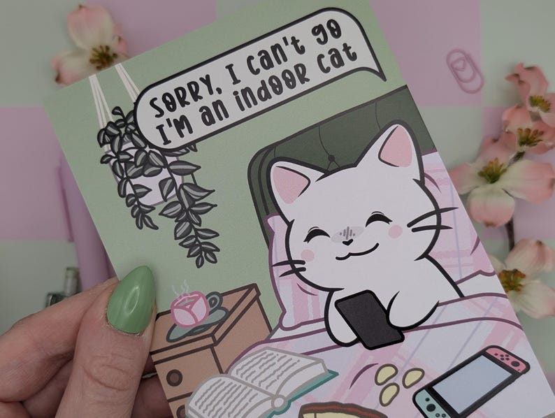 May include: A greeting card with a cartoon cat in bed holding a phone. The card has the text "Sorry, I can't go, I'm an indoor cat" in a speech bubble. The card is light green with a pink and white patterned background.