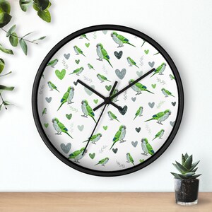 May include: A white clock with black hands and a black frame. The clock face has a repeating pattern of green parakeets and gray hearts.