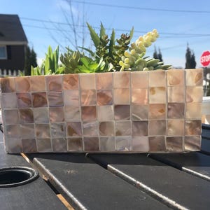 May include: A rectangular planter made of iridescent mosaic tiles in shades of pink and white. The planter is filled with a variety of succulents.