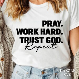 May include: White t-shirt with the text "PRAY. WORK HARD. TRUST GOD. Repeat" in black block letters and script. The shirt is worn with blue jeans and a beige cardigan.