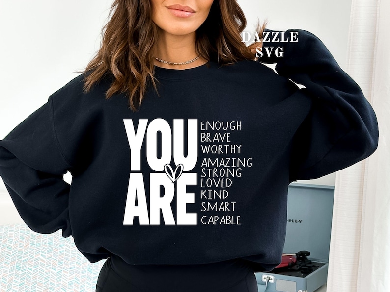 May include: Black sweatshirt with the words "YOU ARE" in large white letters, with a heart symbol. Below, the words "ENOUGH, BRAVE, WORTHY, AMAZING, STRONG, LOVED, KIND, SMART, CAPABLE" are listed. The sweatshirt is a casual style.
