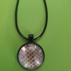 May include: A black cord necklace with a round pendant featuring a brown and white snake skin pattern.