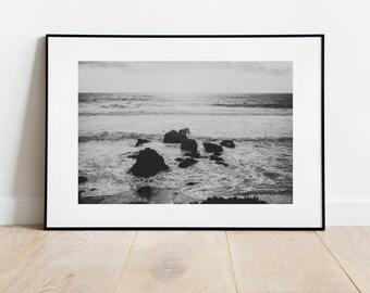 May include: A black and white photograph of a rocky shoreline with waves crashing against the rocks. The photo is framed in a black frame.