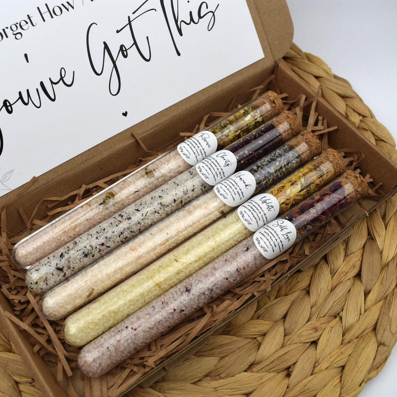 May include: Six glass test tubes filled with bath salts and dried flowers. The test tubes are arranged in a box with a brown paper liner. The text on the labels reads "Rose", "Citrus", "Chamomile", "Lavender", "White Tea", and "Salt Love".
