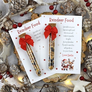 May include: Two clear glass test tubes filled with birdseed, each topped with a cork stopper and a red ribbon bow. Each tube is attached to a white card printed with the text Reindeer Food, a poem, and an illustration of Santa and a reindeer.