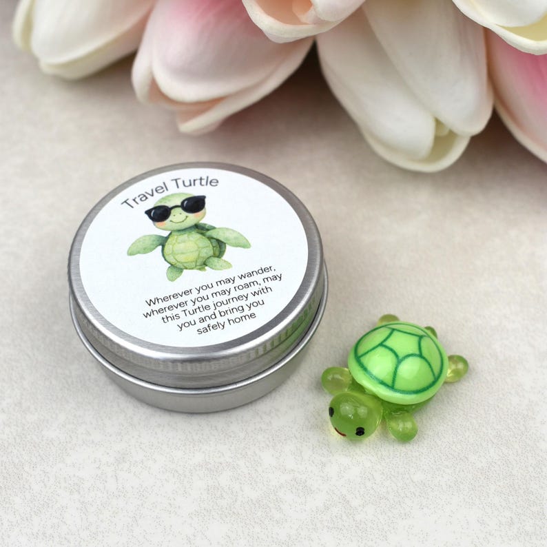 May include: A small, round, silver tin with a "Travel Turtle" label featuring a cartoon turtle wearing sunglasses. Next to the tin is a small, green, glass turtle figurine. The label includes text about safe travels.