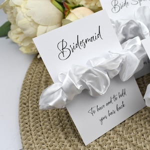 May include: White satin scrunchie with a card that says "Bridesmaid" and "To have and to hold your hair back".