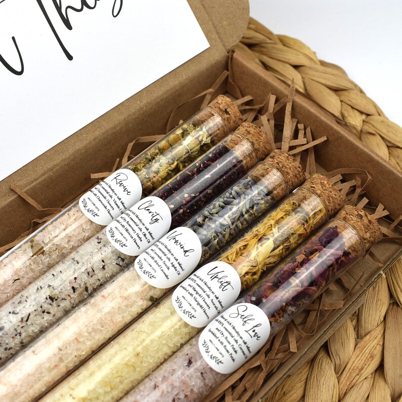 May include: A set of six glass test tubes filled with dried flowers and bath salts. Each tube has a label with a different word: "Revive", "Clarity", "Unwind", "Uplift", "Self Love", and "Soothe".