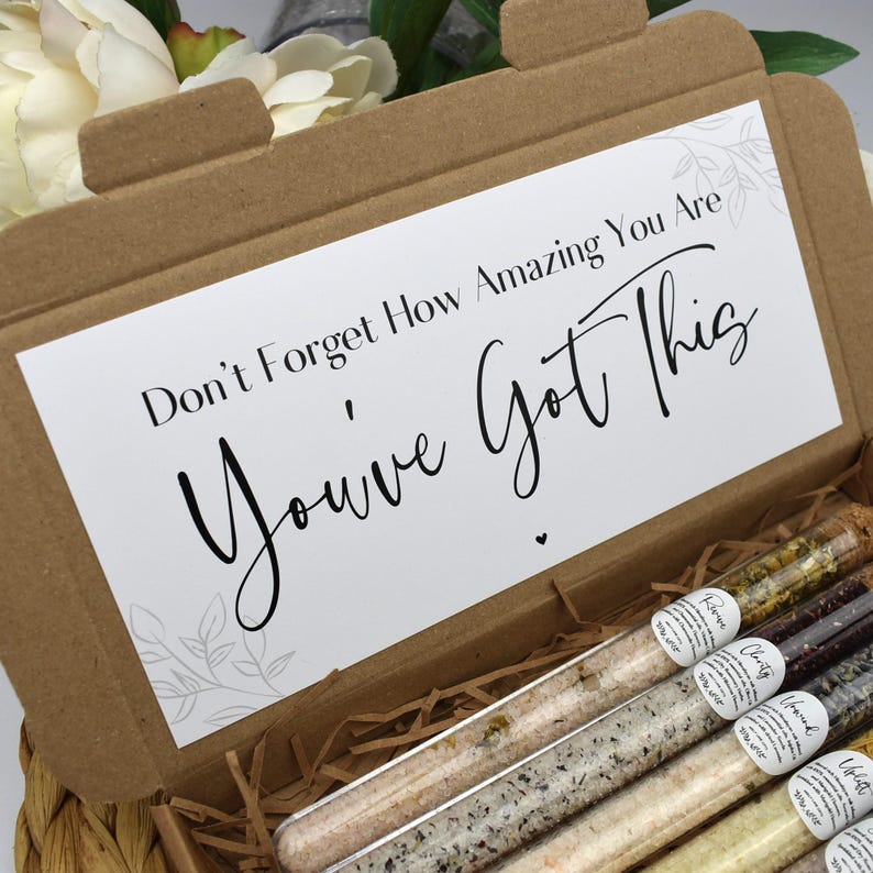 May include: A cardboard box with a white card that reads "Don't Forget How Amazing You Are, You've Got This". The box contains several glass test tubes filled with bath salts.