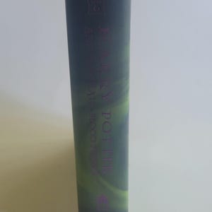 May include: A hardcover book with a dark green and purple cover. The spine features the title "Harry Potter" in purple lettering, along with the author's name and the text "Year 6". The book's edges are white.