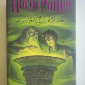 May include: The cover of "Harry Potter and the Half-Blood Prince" by J.K. Rowling. The book has a purple title, with illustrations of Dumbledore, Harry Potter, and a green cauldron.